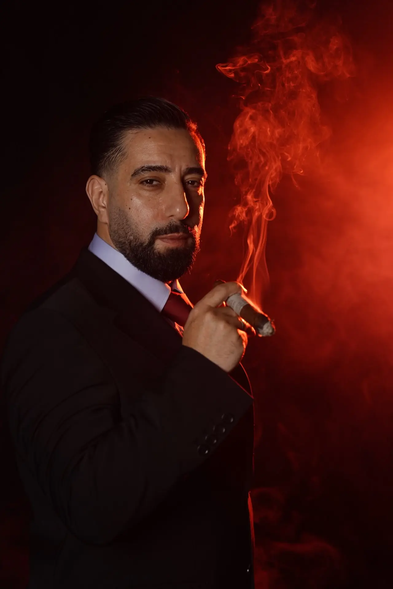 نورسامت ياردميديجي من الجانب، ببدلة سوداء وربطة عنق حمراء، وسط دخان أحمر