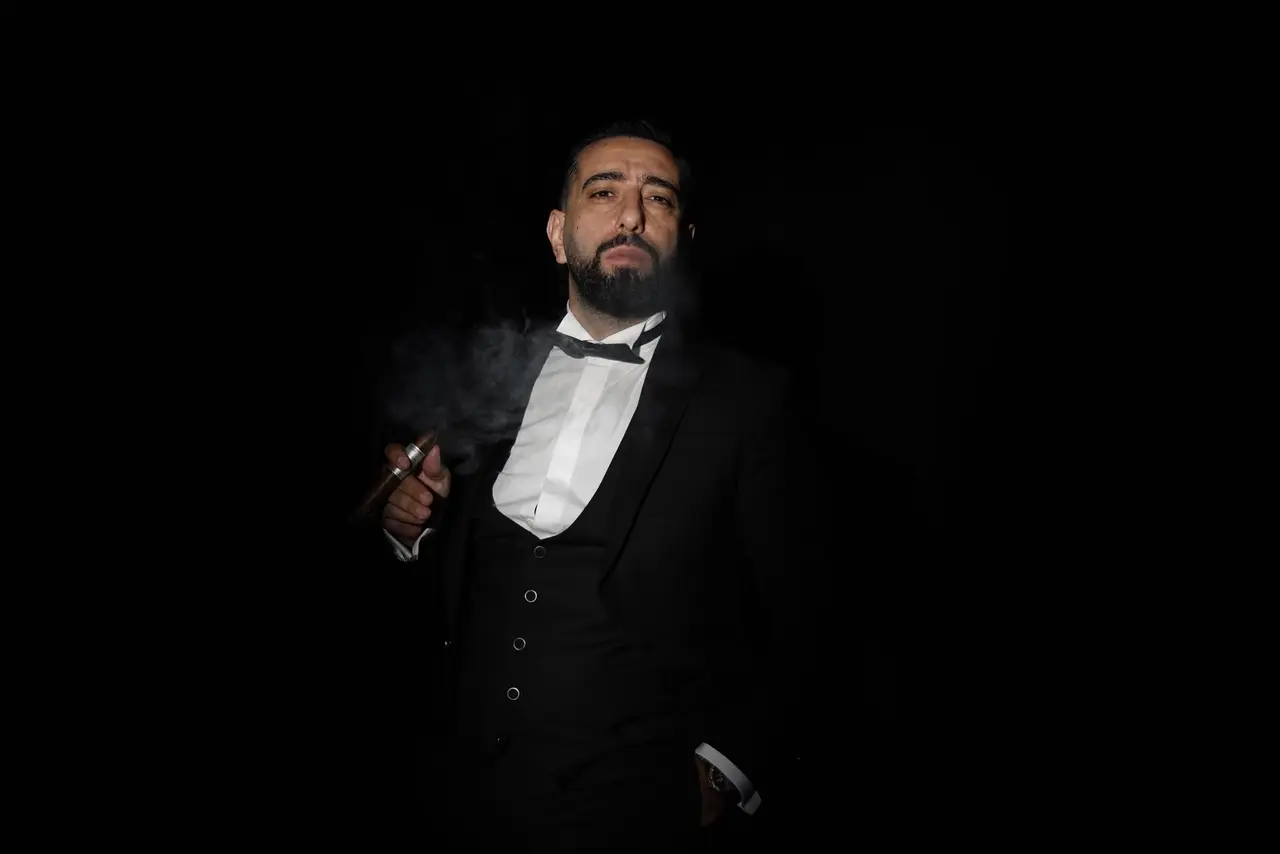 نورسامت ياردميديجي واقفًا وسط الدخان أمام خلفية سوداء