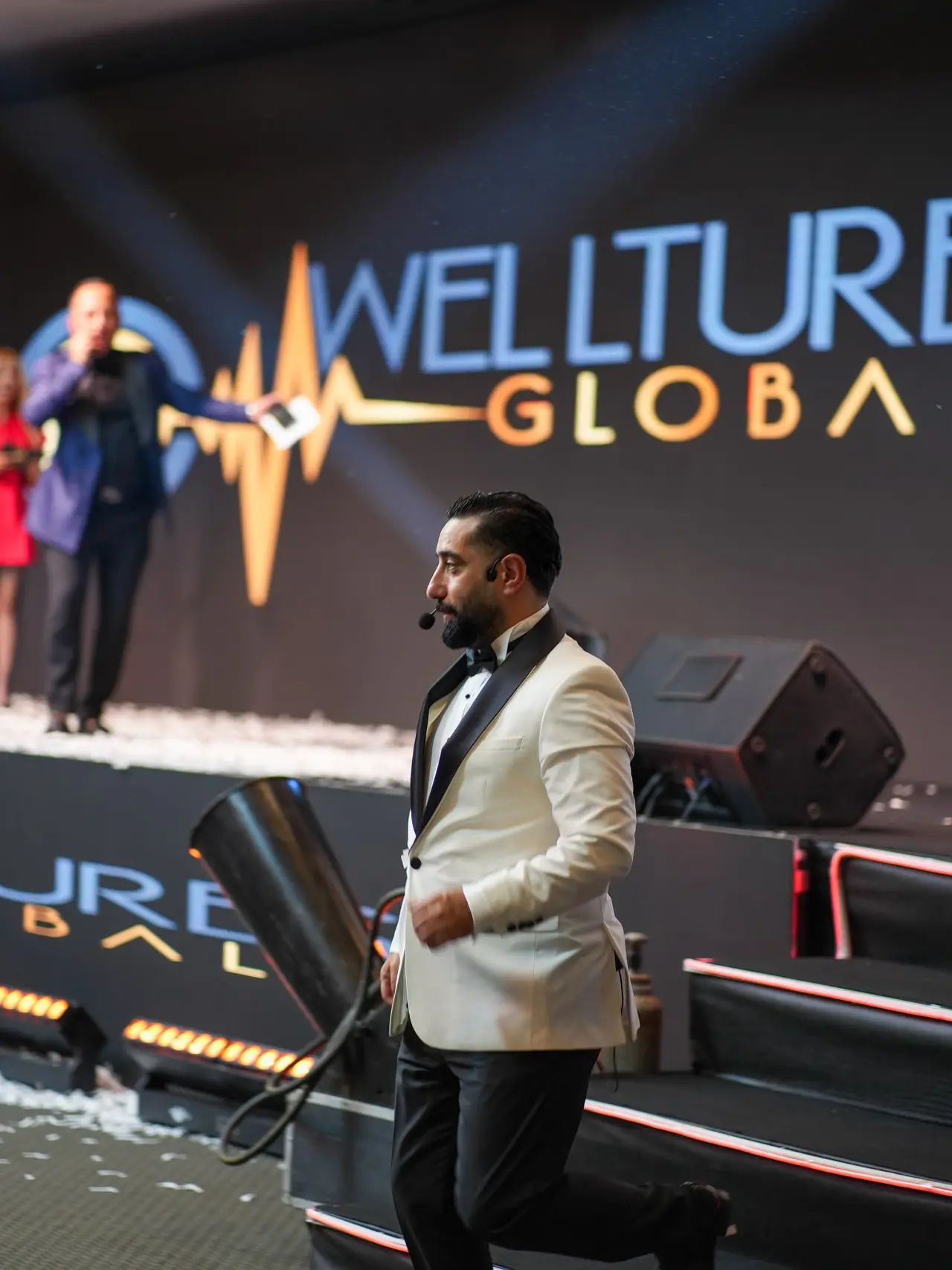 يسير على مسرح Welltures Global ببدلة سهرة بيضاء وسط قصاصات الورق الملونة